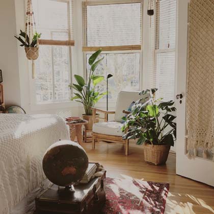Bedroom with a chair near open windows surrounded by plants